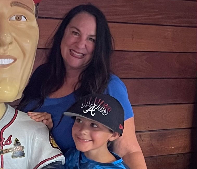 Tracey and her son at a baseball game standing beside a stature of a Braves player