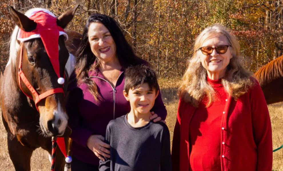 Tracey standing behind her son along with her mother and horses with them